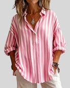 Person wearing a pink and white striped shirt with rolled-up sleeves on a plain background