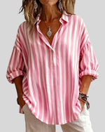 Person wearing a pink and white striped shirt with rolled-up sleeves on a plain background