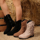 Three pairs of fringed boots in black, brown, and beige on a straw background.