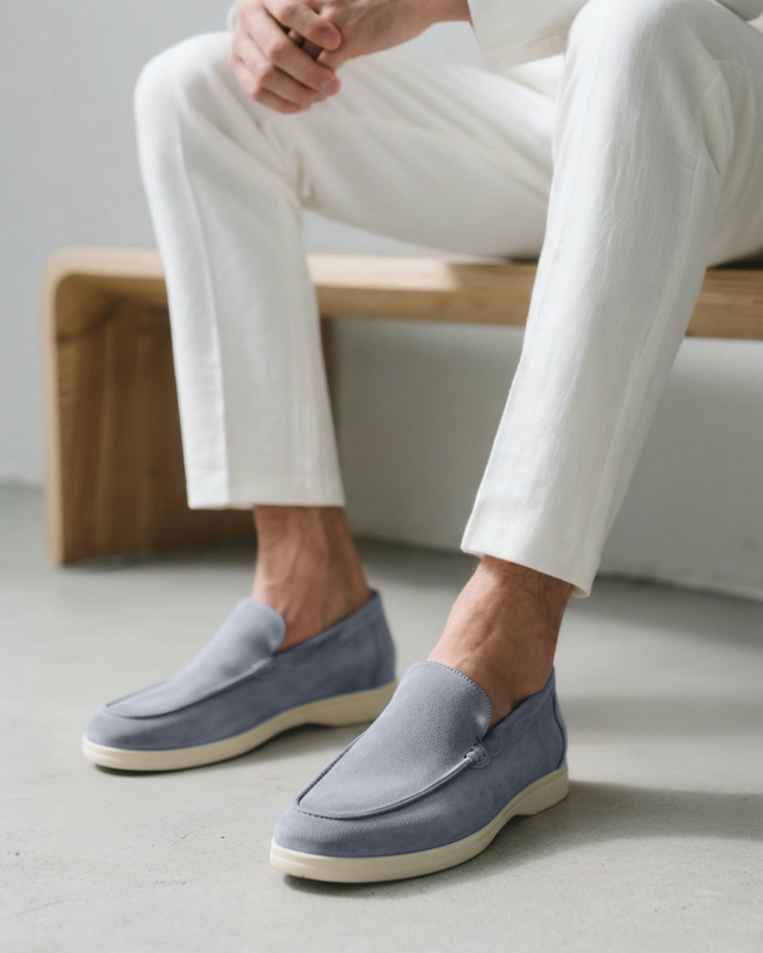 Person wearing light blue loafers with white pants sitting on a wooden bench.
