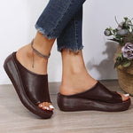 Brown platform sandals worn with blue jeans on a wooden floor.