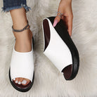 White open-toe sandal with black sole held by a hand on a fluffy white surface