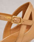 Close-up of a tan sandal with a gold strap and buckle on a light gray background