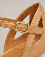 Close-up of a tan sandal with a gold strap and buckle on a light gray background
