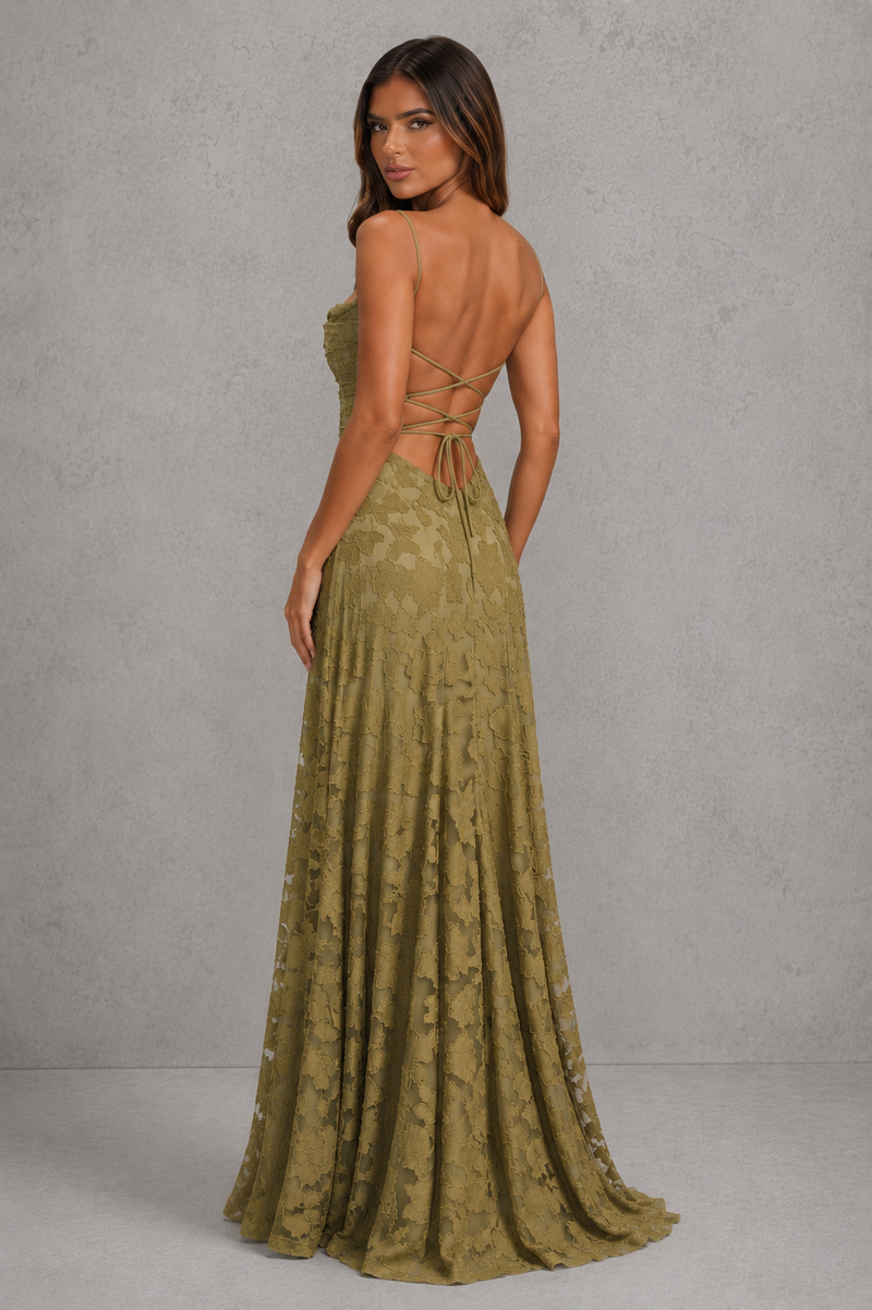 A woman modeling a floor-length olive green lace gown from the back, showing a strapless bodice, open back with tie details, and a full skirt against a textured gray studio backdrop.