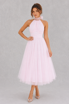 Woman wearing a light pink halter neck dress on a gray background