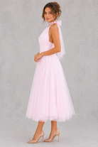 Woman wearing a pink dress with a sheer overlay against a gray background