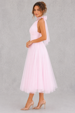 Woman wearing a pink dress with a sheer overlay against a gray background
