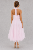 Woman wearing a light pink dress with a sheer halter top on a gray background