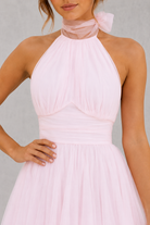 Pink halter neck dress with a bow detail on a plain background