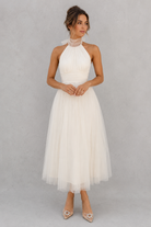 Woman wearing a white halter neck dress against a gray background