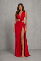A woman modeling a bright red sleeveless maxi dress with a deep V-neckline, side cutouts, and a high thigh slit, standing against a textured gray studio backdrop.