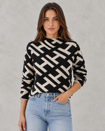 Woman wearing a black and white geometric patterned sweater with light blue jeans against a gray background