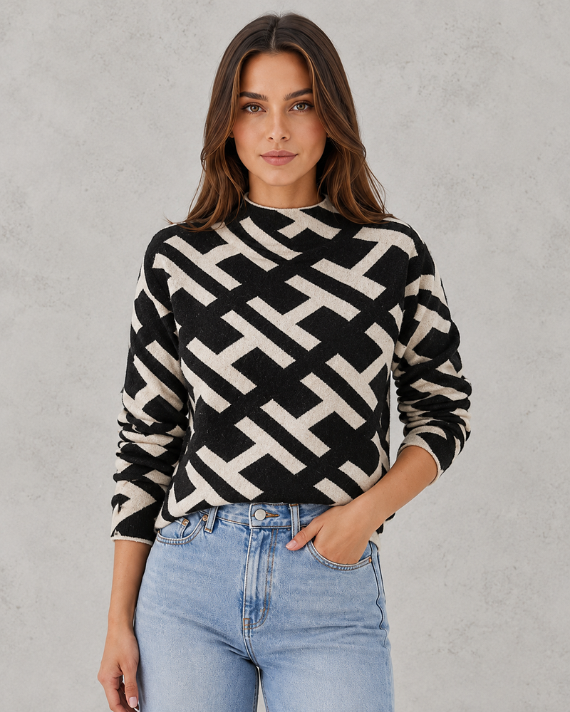 Woman wearing a black and white geometric patterned sweater with light blue jeans against a gray background