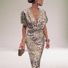 Woman wearing a patterned jumpsuit with gold accessories on a plain background