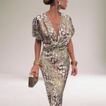 Woman wearing a patterned jumpsuit with gold accessories on a plain background