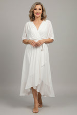 Woman wearing a white dress standing on a wooden deck.