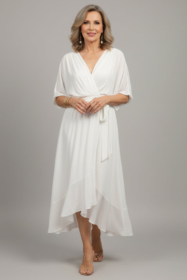 Woman wearing a white dress standing on a wooden deck.