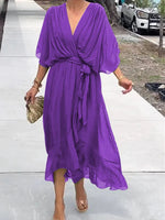 Person wearing a purple dress standing on a sidewalk.