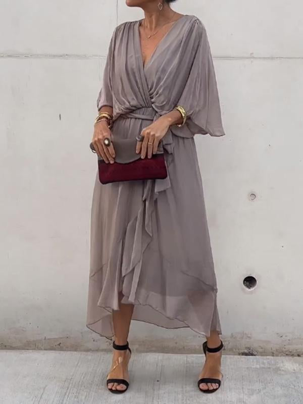 Woman wearing a gray dress with a red clutch against a white wall.