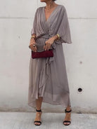 Woman wearing a gray dress with a red clutch against a white wall.