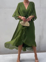 Woman wearing a green dress holding a small handbag against a plain background
