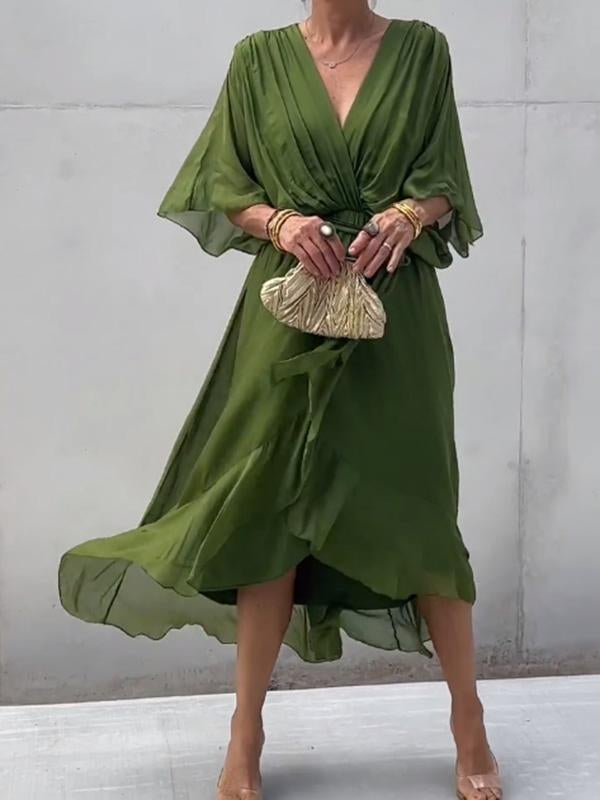 Woman wearing a green dress holding a small handbag against a plain background