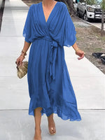 Woman wearing a blue dress standing on a sidewalk.