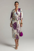 Woman wearing a floral dress with purple accents, holding a matching handbag against a plain background