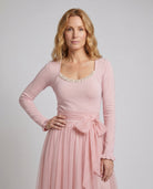 Woman wearing a pink dress with a matching cardigan on a gray background