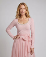 Woman wearing a pink dress with a matching cardigan on a gray background