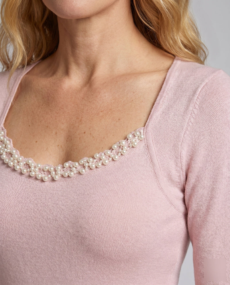 Close-up of a pink top with pearl detailing on a plain background