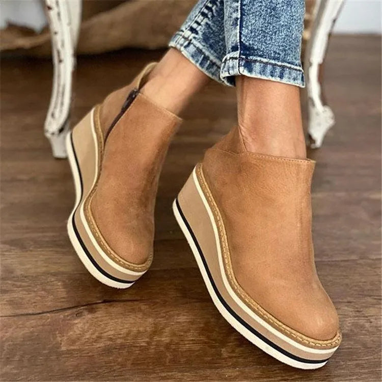 Tan slip-on platform shoes worn with rolled-up jeans on a wooden floor.