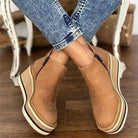 Brown platform shoes worn with blue jeans on a wooden floor.
