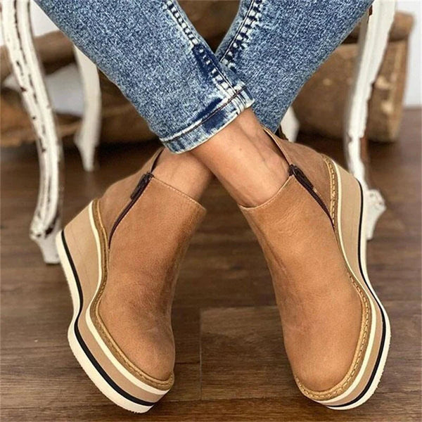 Brown platform shoes worn with blue jeans on a wooden floor.
