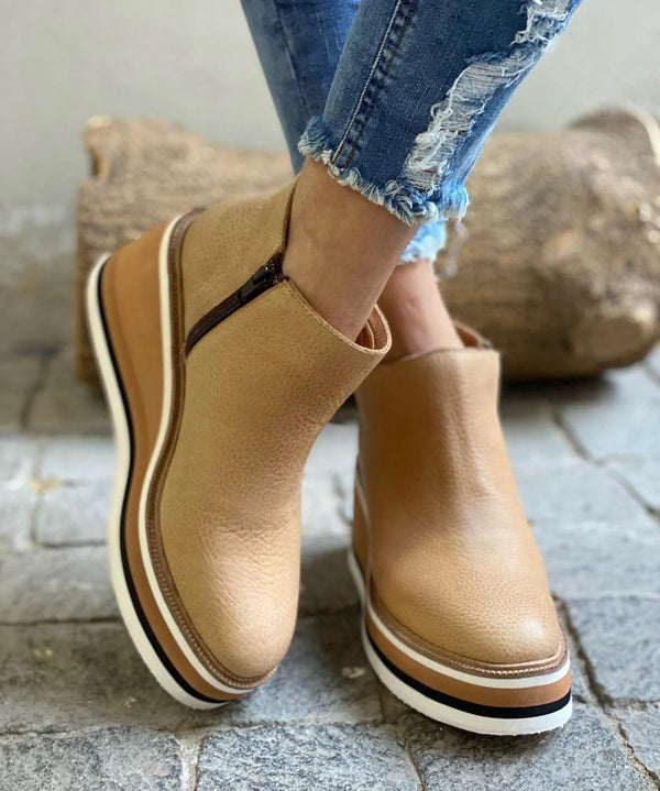 Tan platform shoes worn with blue jeans on a stone floor.