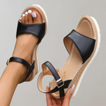 Black and beige sandals with a strap held by a hand on a gray background