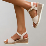 Beige wedge sandals with jute sole worn by a person on a light gray background