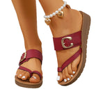 Close-up of a sandal with a red strap and gold buckle on a white background