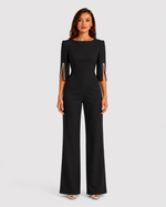 Woman wearing a black jumpsuit with metallic cuffs on a white background
