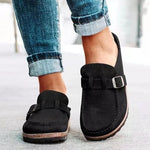 Black loafers with buckles worn with rolled-up jeans on a light background