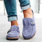 Blue suede loafers with buckles worn with rolled-up jeans on a light background