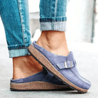 Blue clogs with cork soles worn with rolled-up jeans on a light background