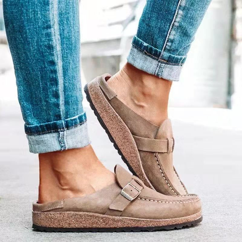 Brown sandals worn with rolled-up blue jeans on a light background
