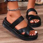 Black sandals worn on a wooden floor with a person's leg visible.