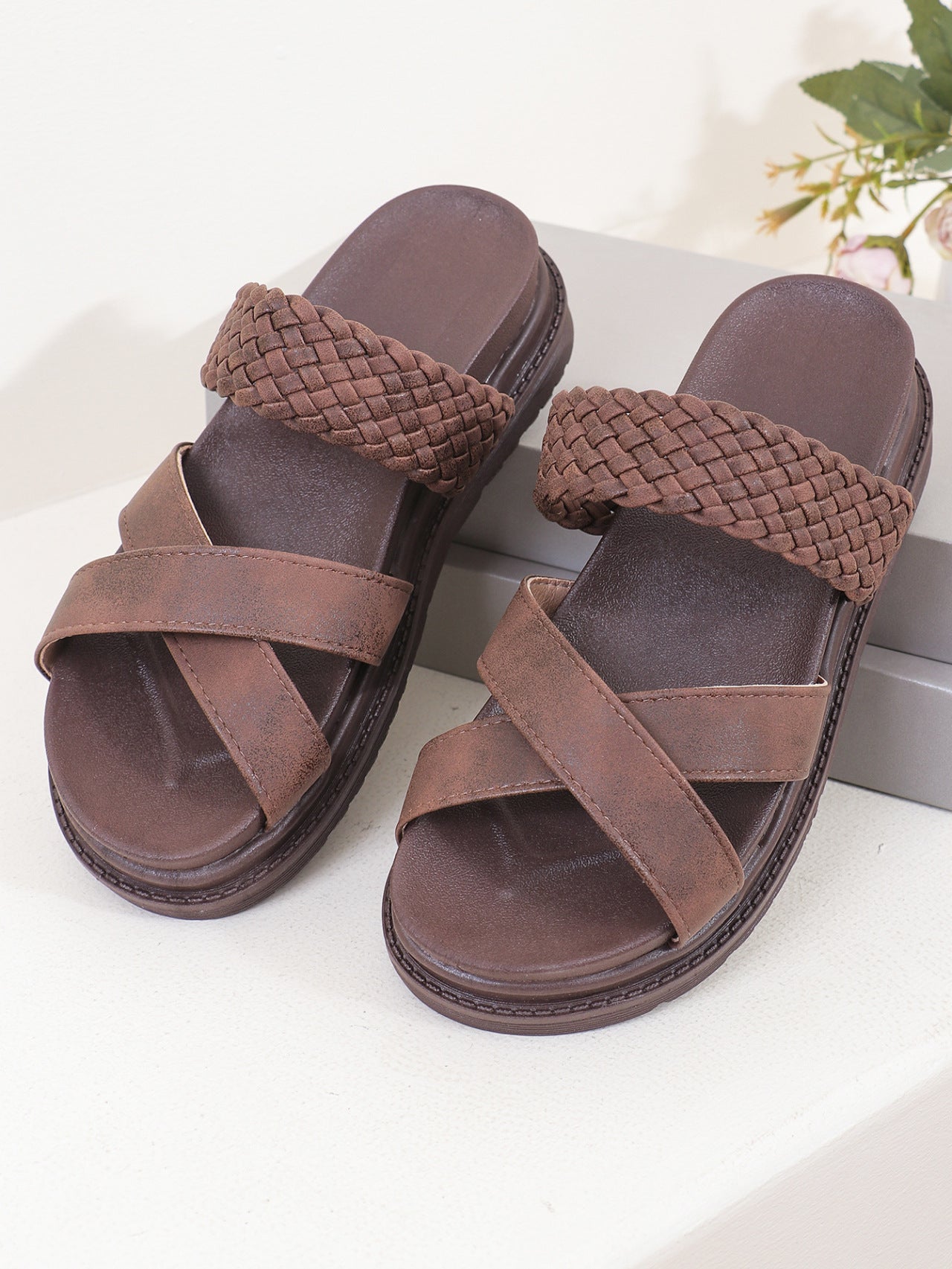 Pair of brown sandals with woven straps on a white surface.