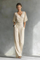 Woman wearing a beige jumpsuit standing against a textured gray wall.