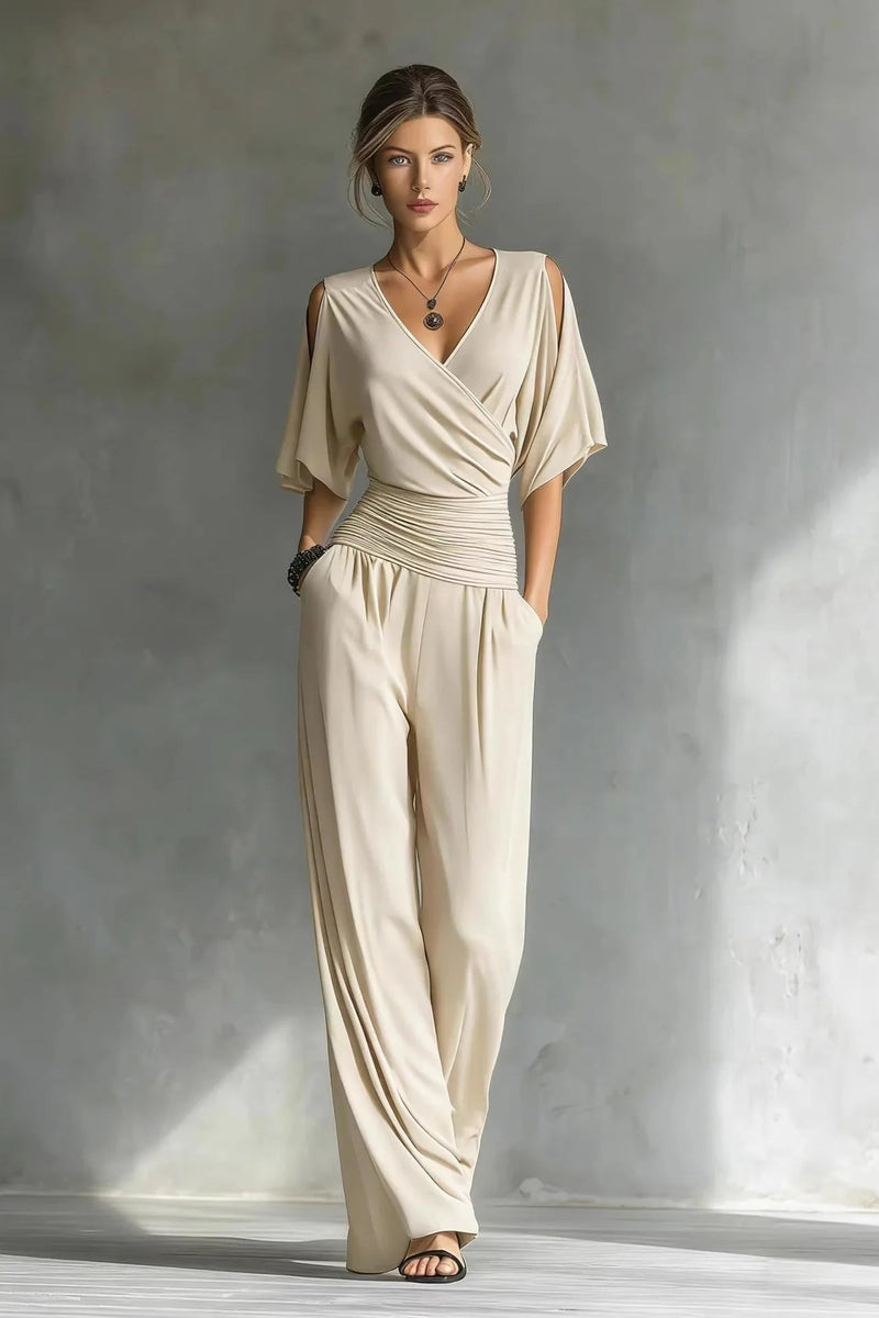 Woman wearing a beige jumpsuit standing against a textured gray wall.