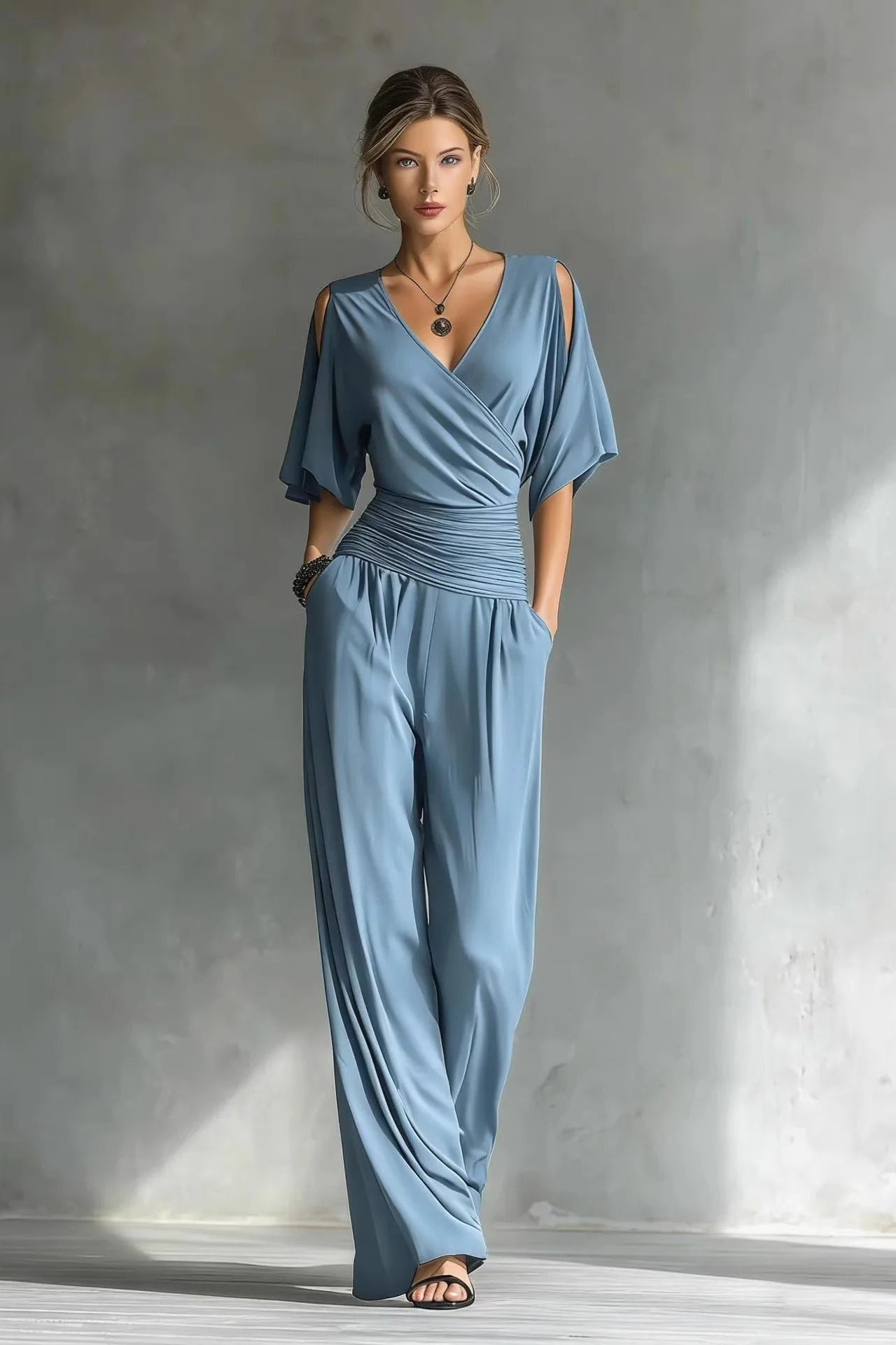Woman wearing a blue jumpsuit standing against a gray wall.