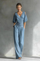 Woman wearing a blue jumpsuit standing against a gray wall.